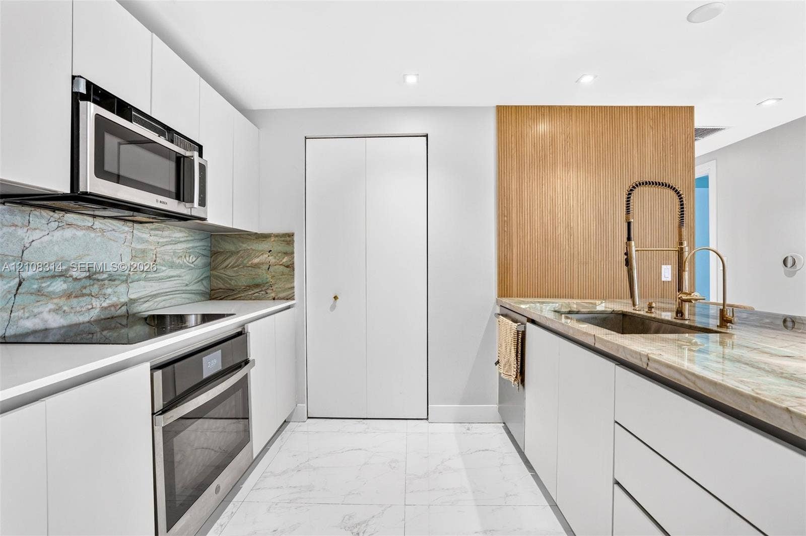 488 NE 18th Street, #4010, Miami, FL 33132 Modern kitchen featuring flat-panel white cabinetry, stone slab countertops, integrated stainless steel appliances, and wood-finish accent paneling with a gooseneck faucet