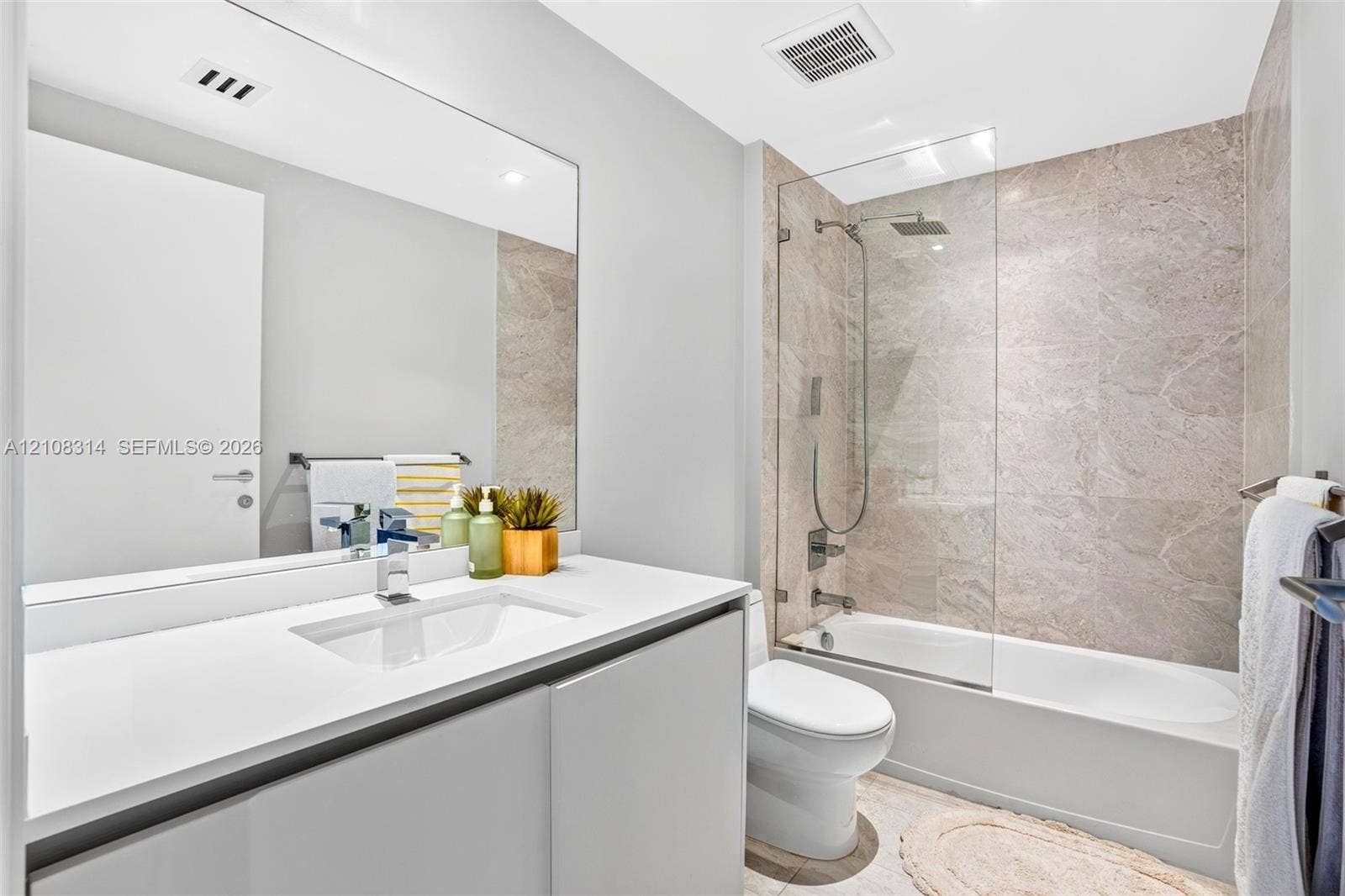488 NE 18th Street, #4010, Miami, FL 33132 Bathroom featuring a floating vanity with a stone countertop, an integrated rectangular sink, a frameless glass shower panel, and stone-tile tub surround