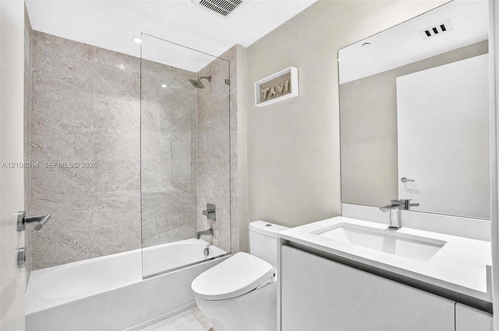 488 NE 18th Street, #4010, Miami, FL 33132 Bathroom featuring a vanity with a white countertop and integrated sink, frameless glass shower enclosure, stone-finish tile surround, and large wall-mounted mirror