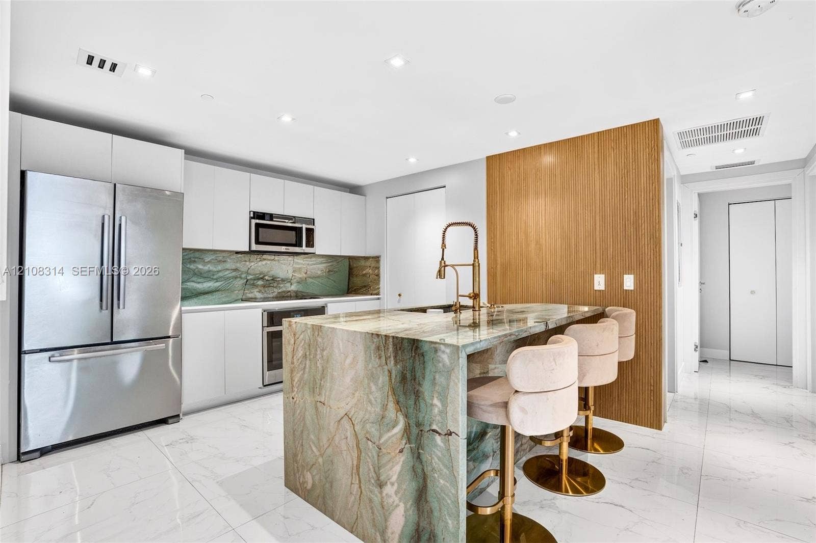 488 NE 18th Street, #4010, Miami, FL 33132 Kitchen featuring flat-panel white cabinetry, stone-clad waterfall island, matching stone backsplash, wood-finish accent wall, and stainless steel appliances