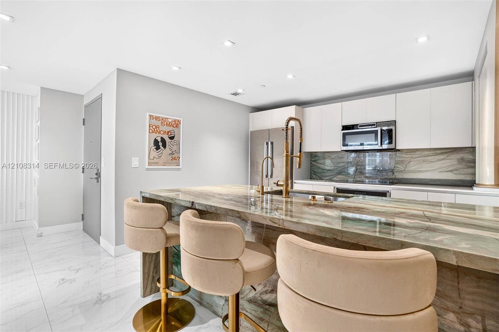488 NE 18th Street, #4010, Miami, FL 33132 Kitchen featuring a stone waterfall island with a metal gooseneck faucet, white flat-panel cabinetry, a matching stone backsplash, stainless steel appliances, and large-format tile flooring