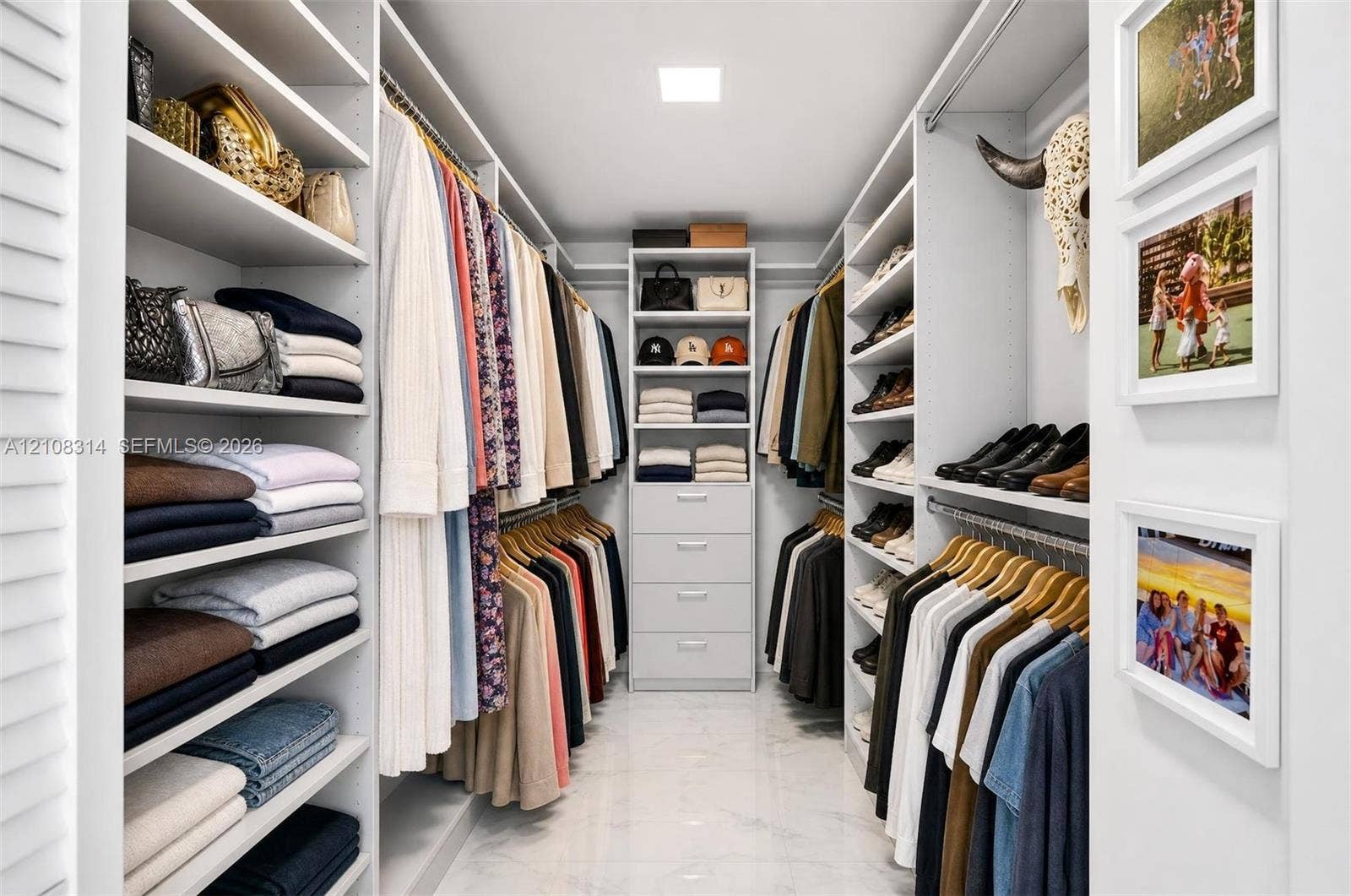 488 NE 18th Street, #4010, Miami, FL 33132 Custom walk-in closet featuring extensive built-in white shelving, integrated clothing rods, a central storage tower with four pull-out drawers, and polished stone-finish flooring