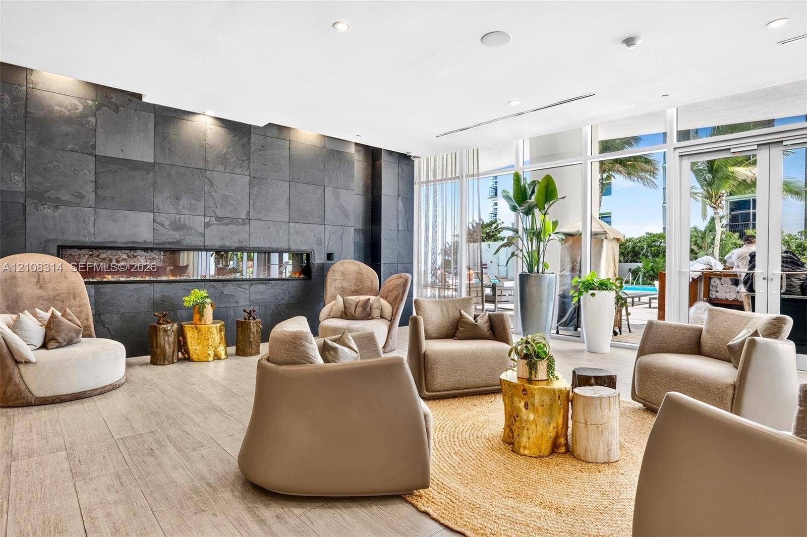 488 NE 18th Street, #4010, Miami, FL 33132 Large-format stone tile accent wall featuring a built-in linear fireplace, wood-finish flooring, and floor-to-ceiling glass paneling