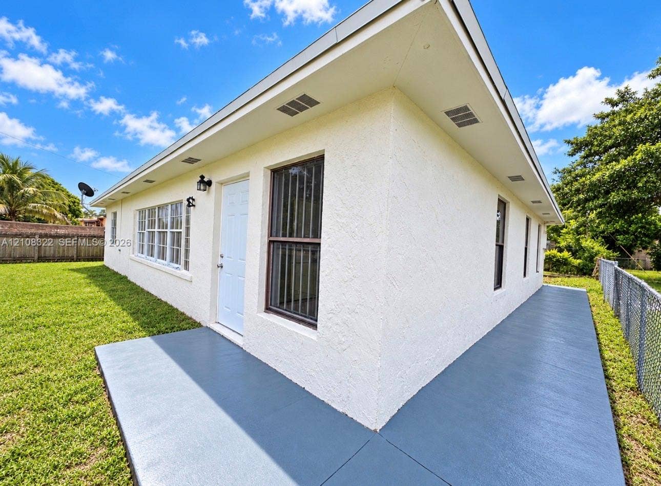 722 NW 7th Avenue, Homestead, FL 33030 Exterior featuring a textured stucco finish, painted concrete patio, white door, multi-pane windows, and inset soffit lighting