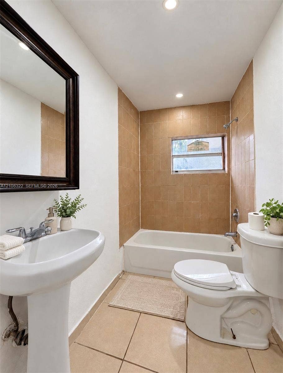 722 NW 7th Avenue, Homestead, FL 33030 Bathroom featuring a pedestal sink, framed wall mirror, tiled bathtub surround, and tile flooring