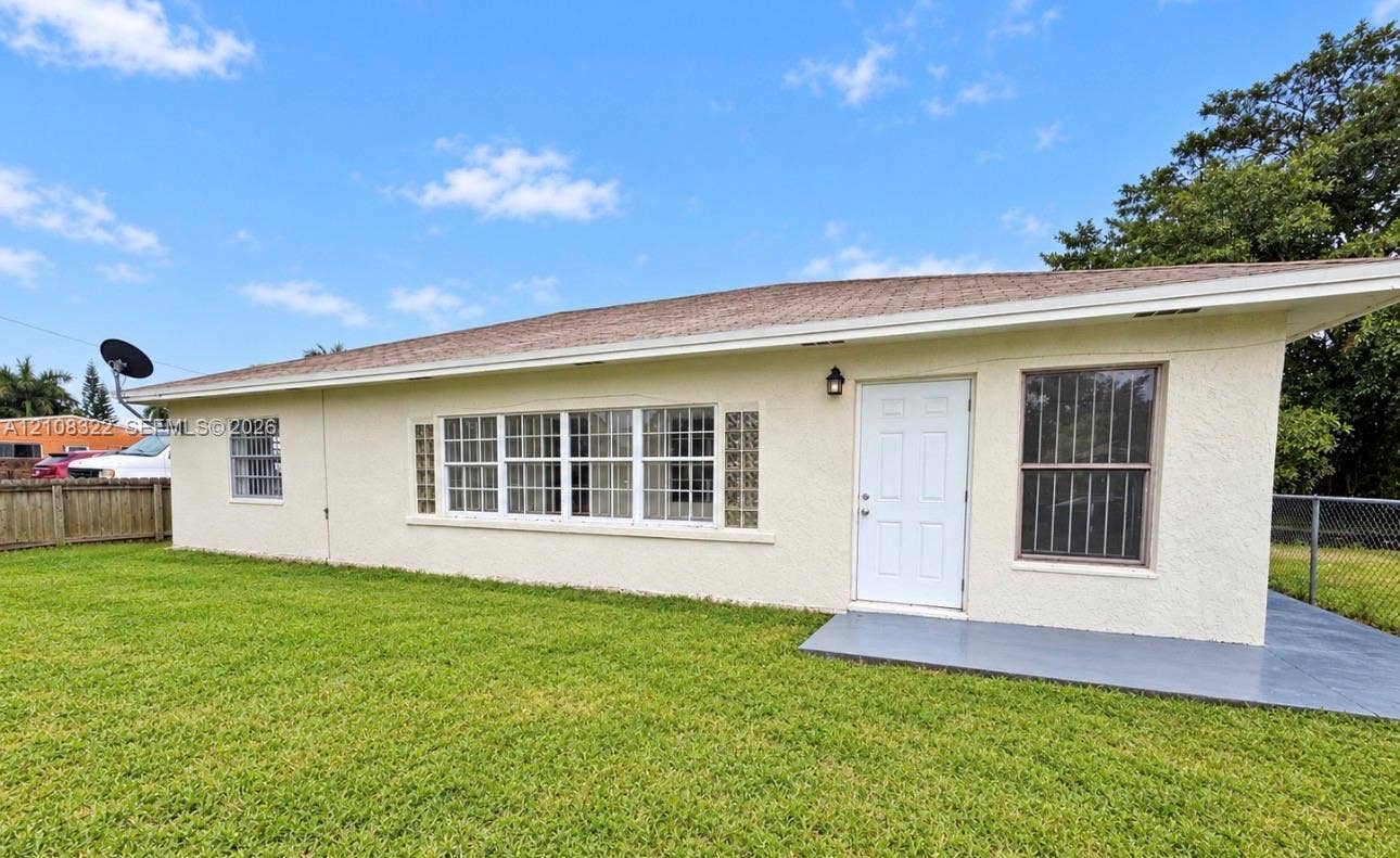 722 NW 7th Avenue, Homestead, FL 33030 Stucco exterior featuring an expansive multi-pane window configuration, glass block accents, covered concrete patio, and mature lawn