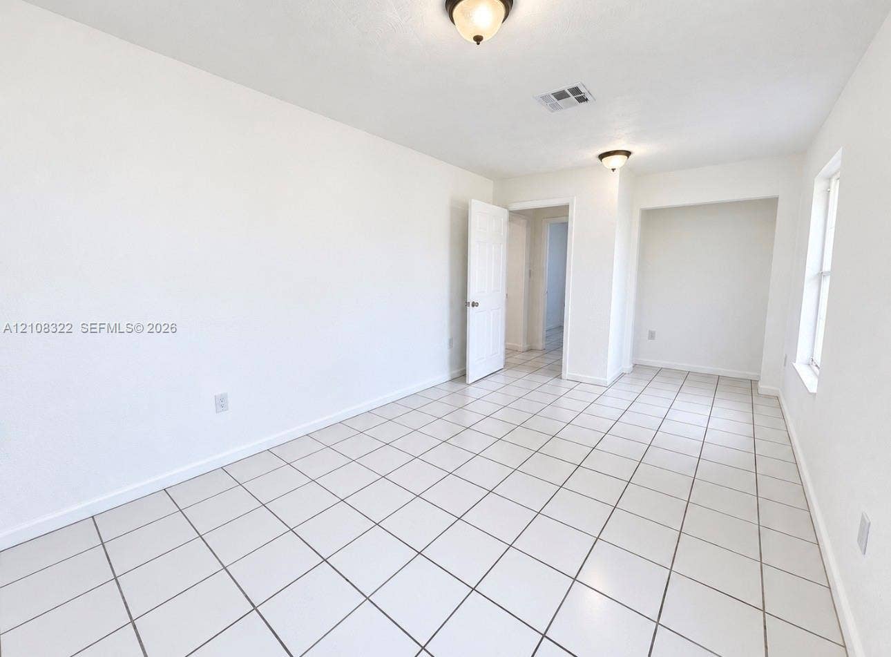 722 NW 7th Avenue, Homestead, FL 33030 Room featuring white ceramic tile flooring, recessed wall niche, two flush-mount light fixtures, and a six-panel door