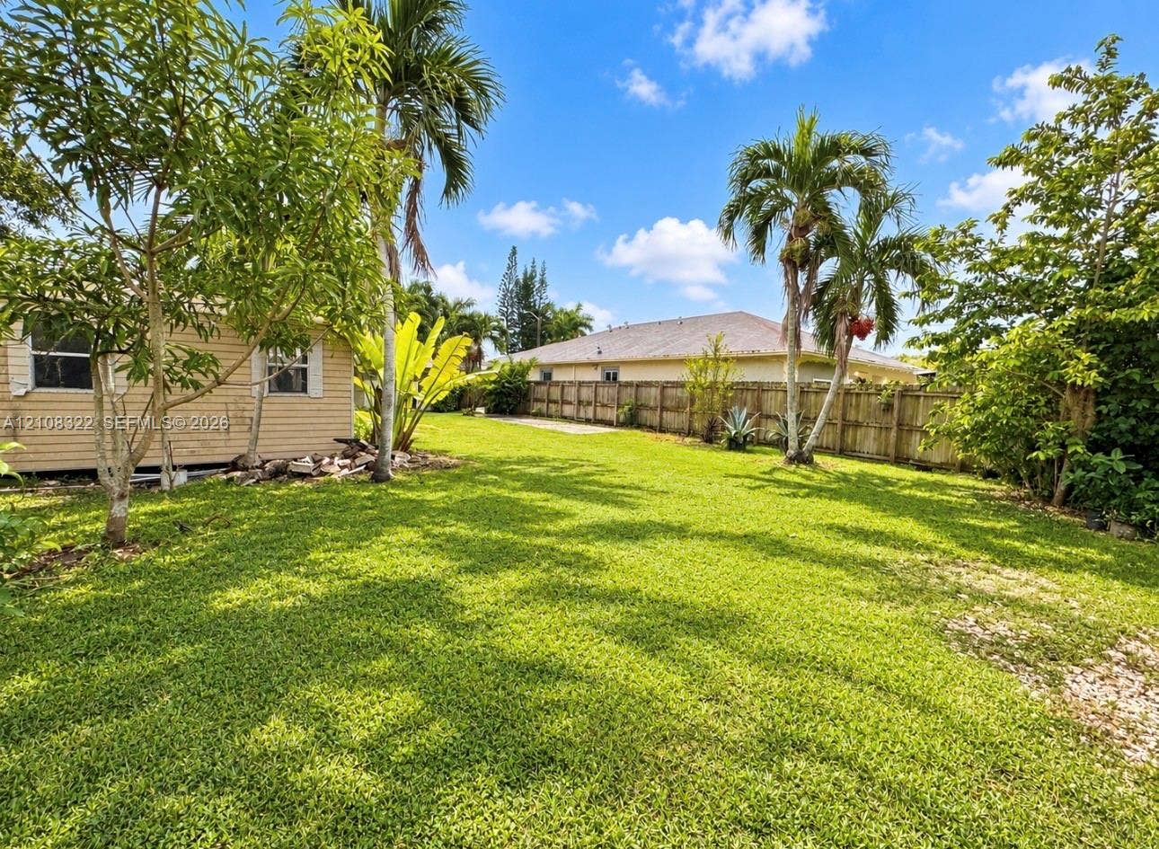 722 NW 7th Avenue, Homestead, FL 33030 Expansive backyard featuring a lush grass lawn, mature palm trees, diverse native vegetation, and a full-height wood perimeter fence