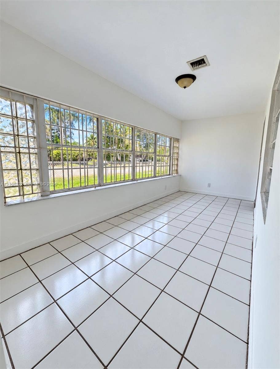 722 NW 7th Avenue, Homestead, FL 33030 Enclosed space featuring square ceramic tile flooring, an expansive wall of multi-pane windows with metal security bars, glass block side accents, and a flush-mount ceiling light fixture