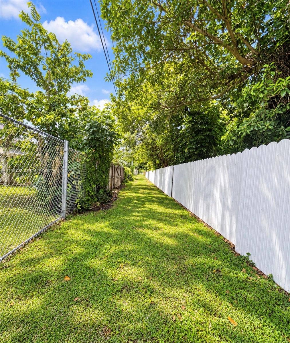 722 NW 7th Avenue, Homestead, FL 33030 Grassy exterior area featuring a white scalloped-top vinyl fence, chain-link perimeter fencing, and mature trees