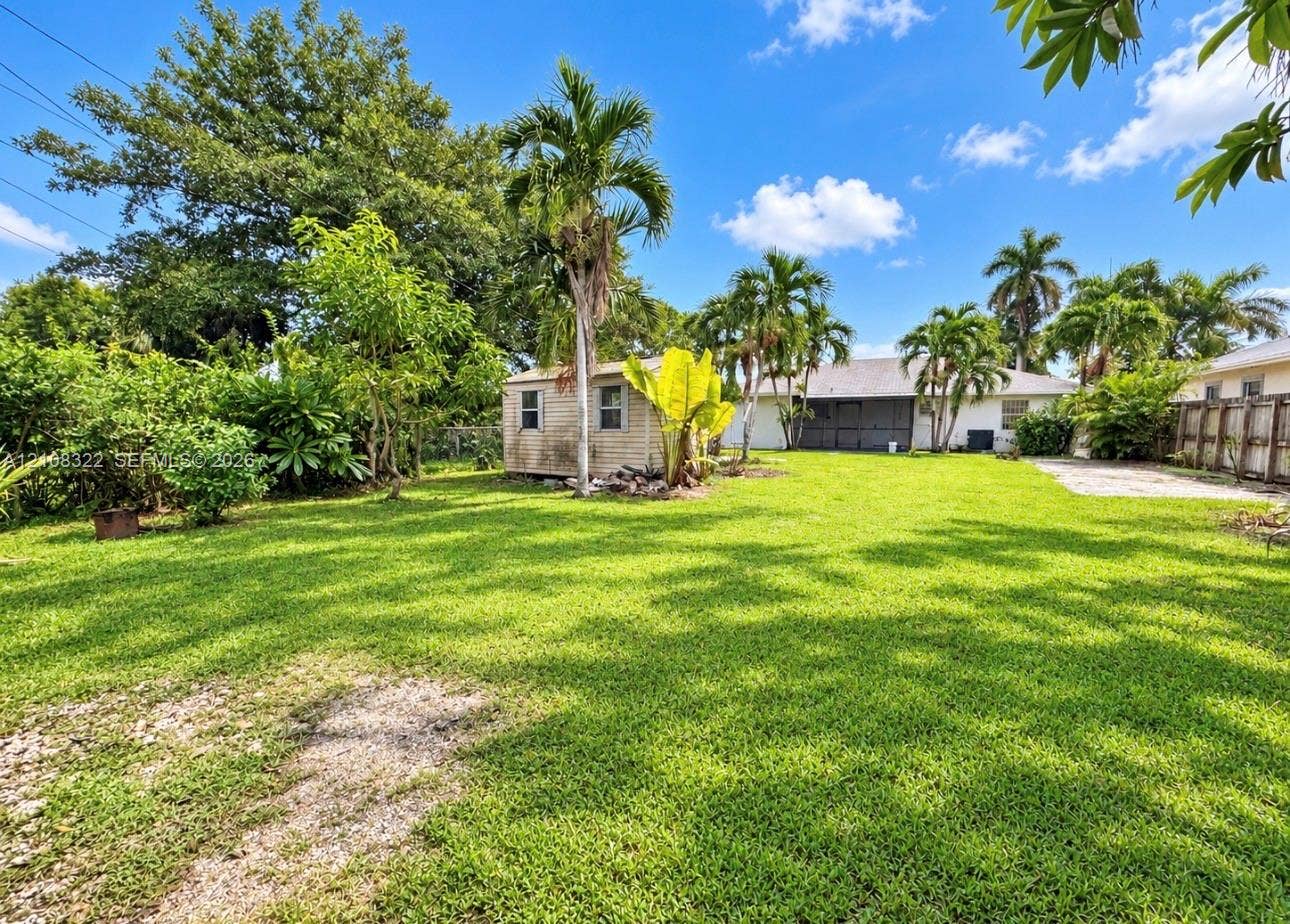 722 NW 7th Avenue, Homestead, FL 33030 Expansive backyard featuring a large grass lawn, mature palm trees, detached storage structure, and perimeter fencing