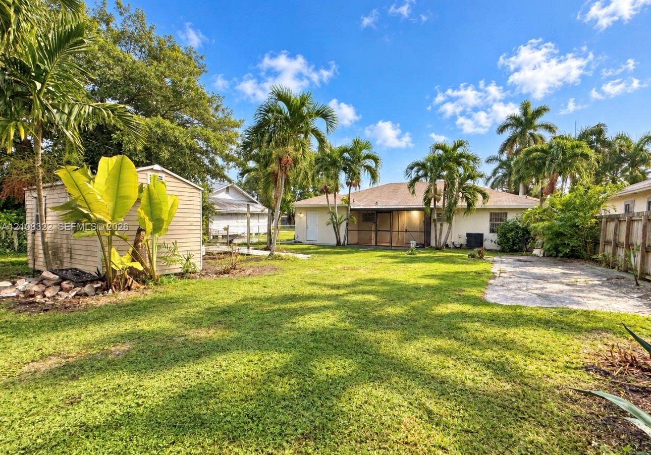 722 NW 7th Avenue, Homestead, FL 33030 Expansive backyard featuring a detached storage shed, screen-enclosed patio, gravel driveway area, and mature palm trees