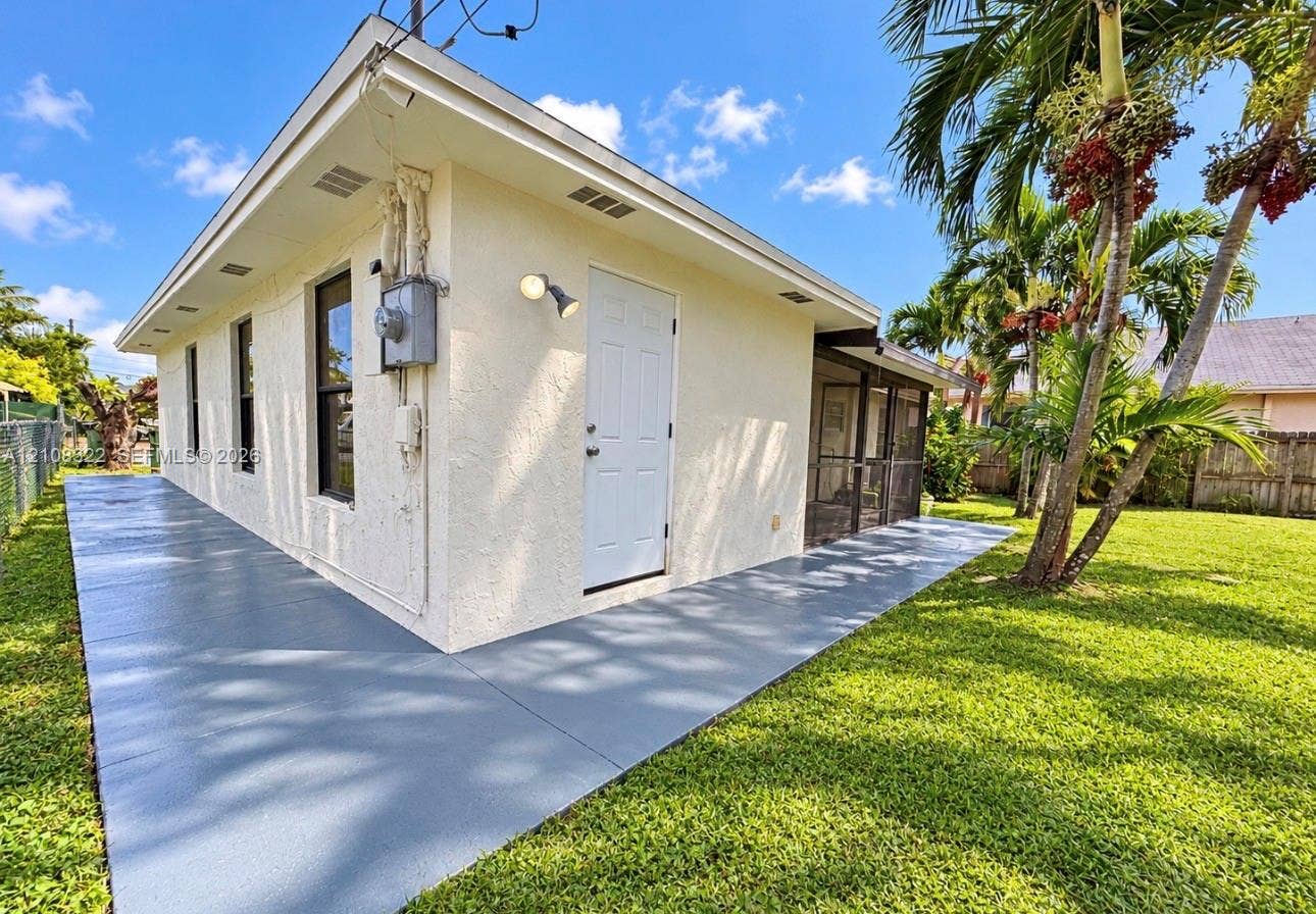 722 NW 7th Avenue, Homestead, FL 33030 Stucco exterior featuring a wraparound concrete patio, screened-in porch, and expansive lawn with mature palm trees