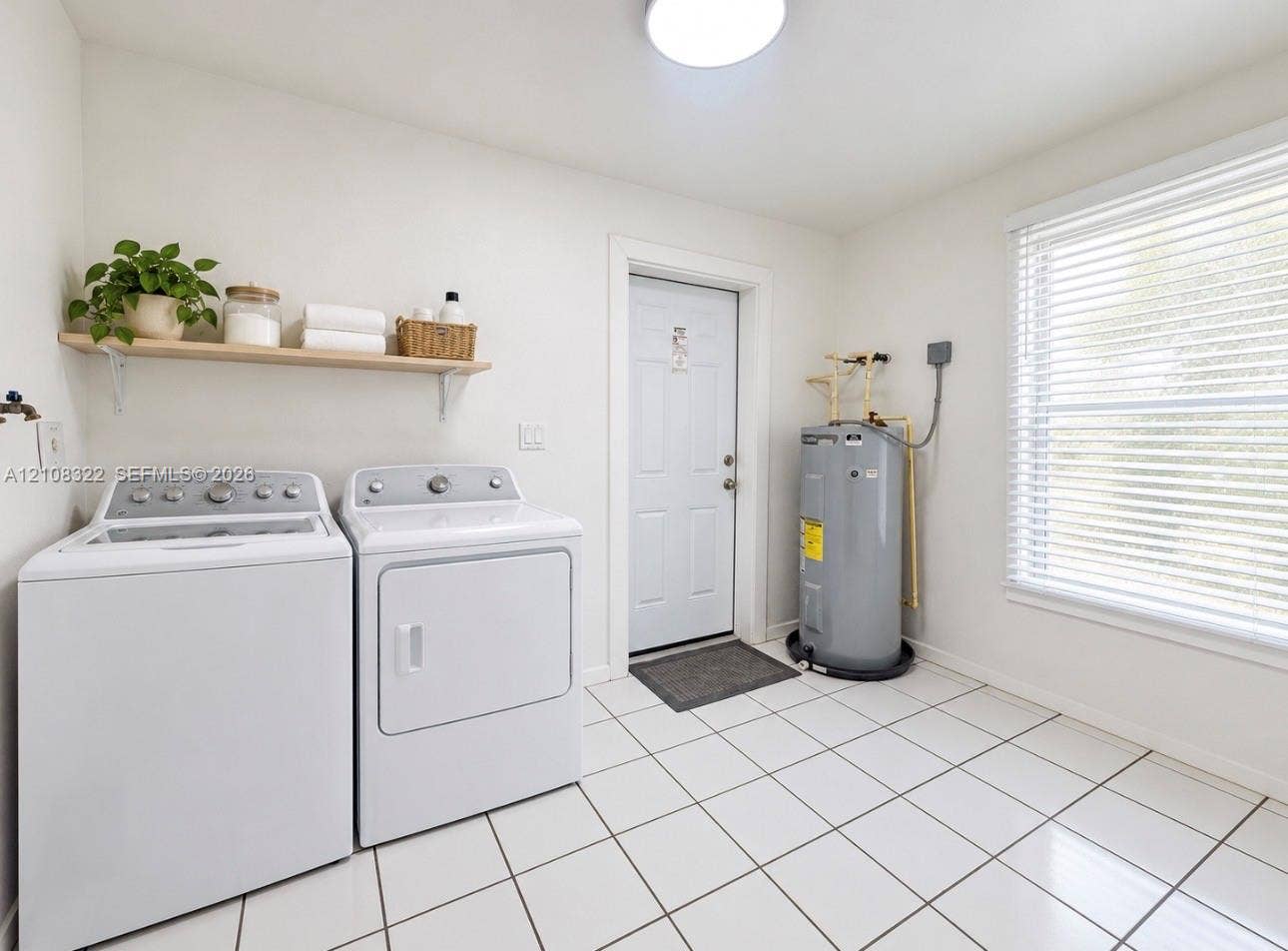 722 NW 7th Avenue, Homestead, FL 33030 Utility space featuring white ceramic tile flooring, a window with horizontal blinds, a solid-panel exterior door, and a mounted wall shelf