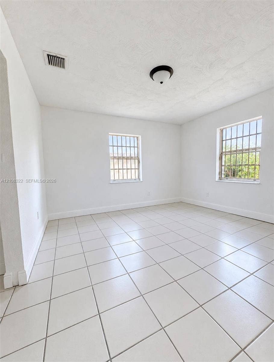 722 NW 7th Avenue, Homestead, FL 33030 Neutral interior space featuring large-format ceramic tile flooring, two windows with metal security bars, and a central flush-mount ceiling fixture
