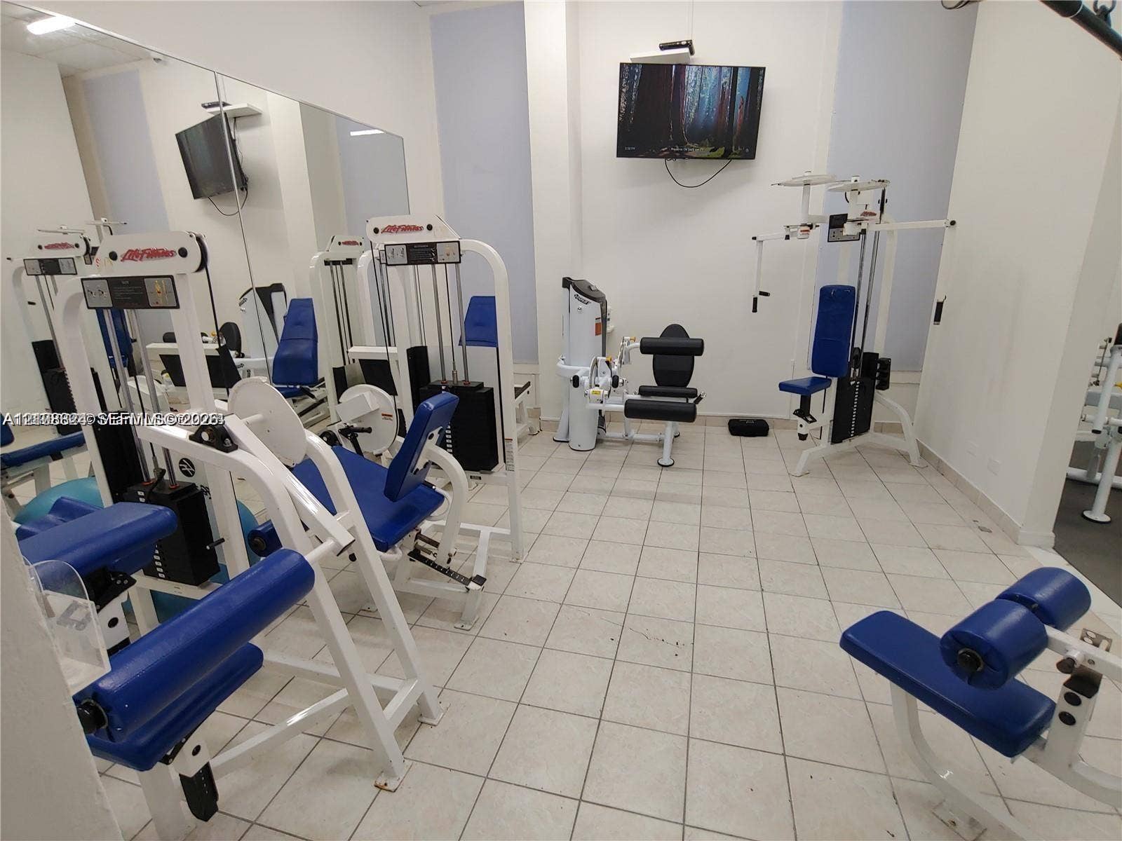 6039 Collins Avenue, #1208, Miami Beach, FL 33140 Fitness center featuring large wall-mounted mirrors and ceramic tile flooring