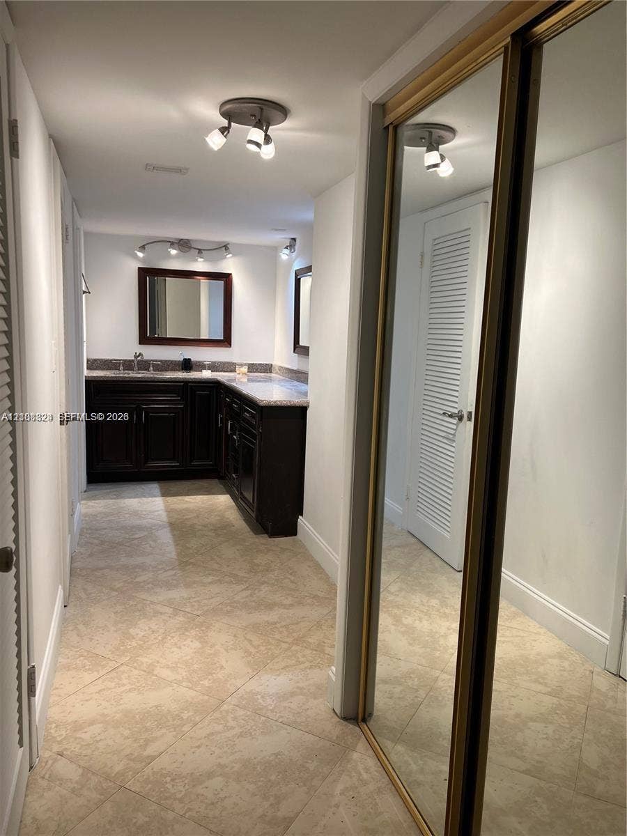 6039 Collins Avenue, #1208, Miami Beach, FL 33140 Dark-finish built-in vanity with a light-toned countertop, tile flooring, mirrored sliding closet doors, and multi-directional track lighting