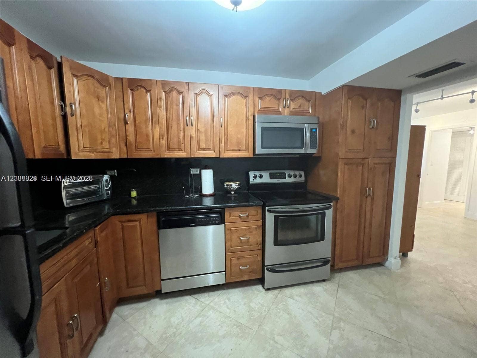 6039 Collins Avenue, #1208, Miami Beach, FL 33140 Kitchen featuring stained wood cabinetry, stone countertops, and stainless steel appliances including a built-in microwave, range, and dishwasher