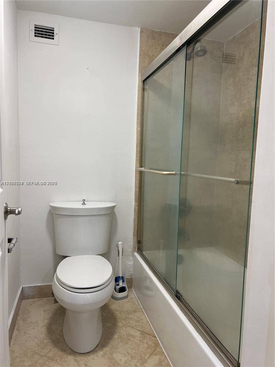 6039 Collins Avenue, #1208, Miami Beach, FL 33140 Full bathroom featuring a glass-enclosed shower, stone-finish tile flooring, neutral wall tile surround, and a standard porcelain toilet