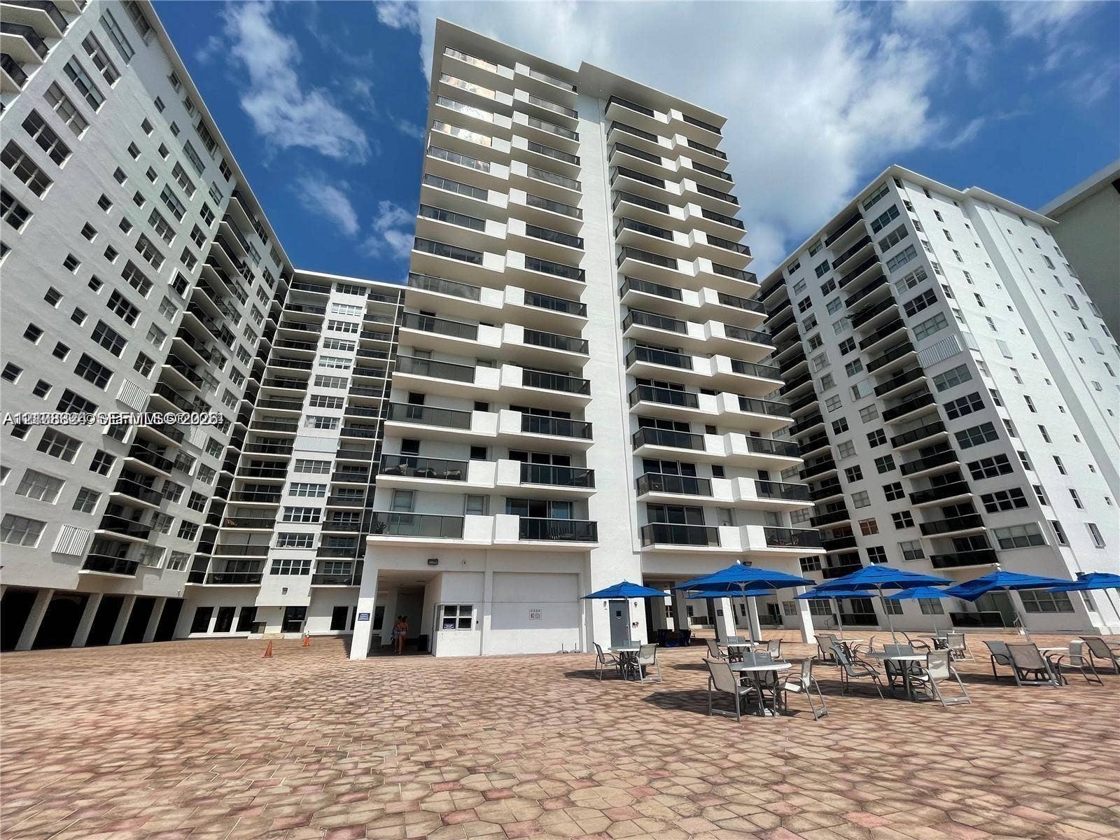 6039 Collins Avenue, #1208, Miami Beach, FL 33140 High-rise residential exterior featuring stacked private balconies, neutral facade, and a paved stone courtyard