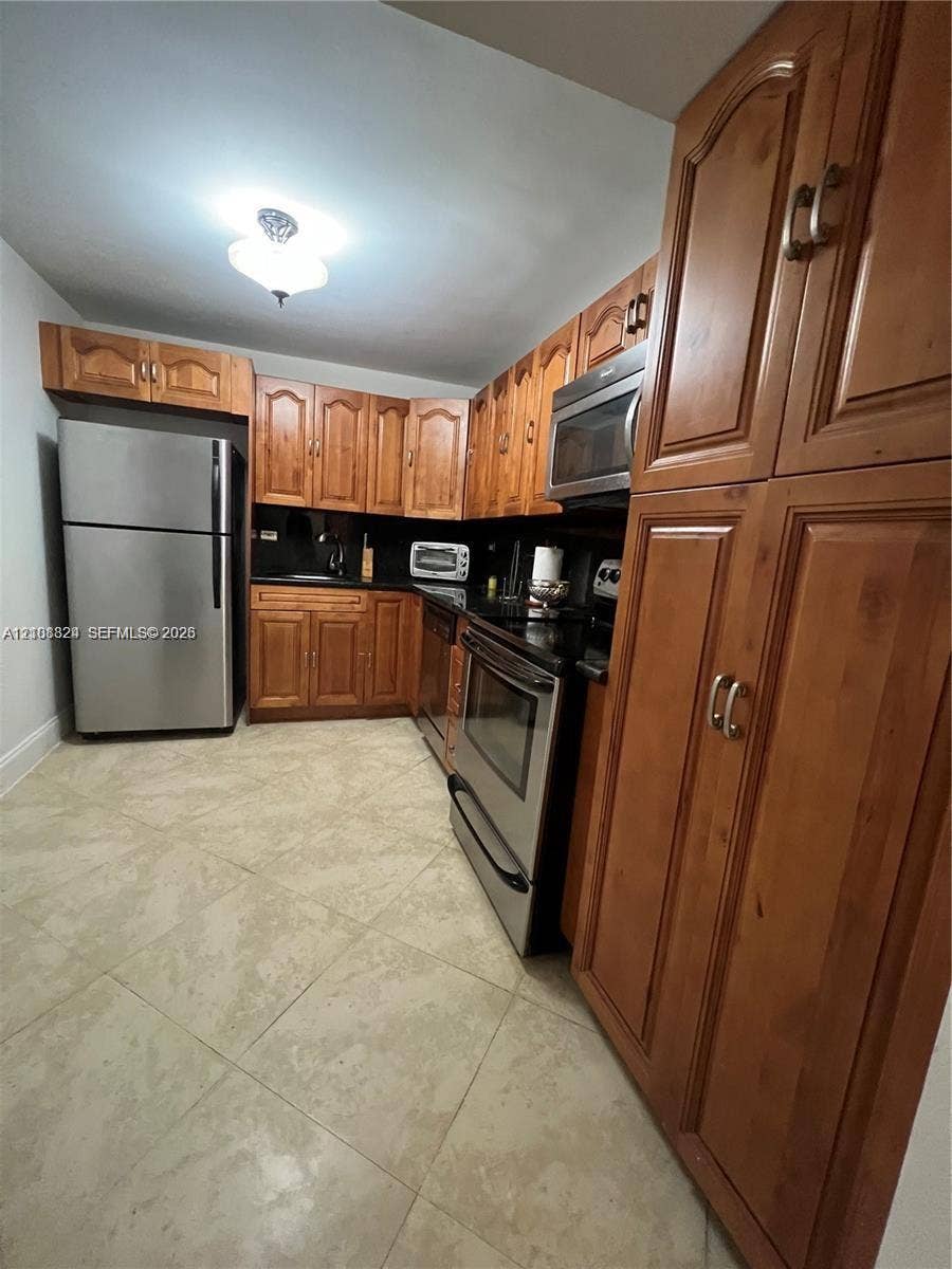 6039 Collins Avenue, #1208, Miami Beach, FL 33140 Kitchen featuring stained wood cabinetry, stainless steel appliances, dark stone countertops, and tile flooring