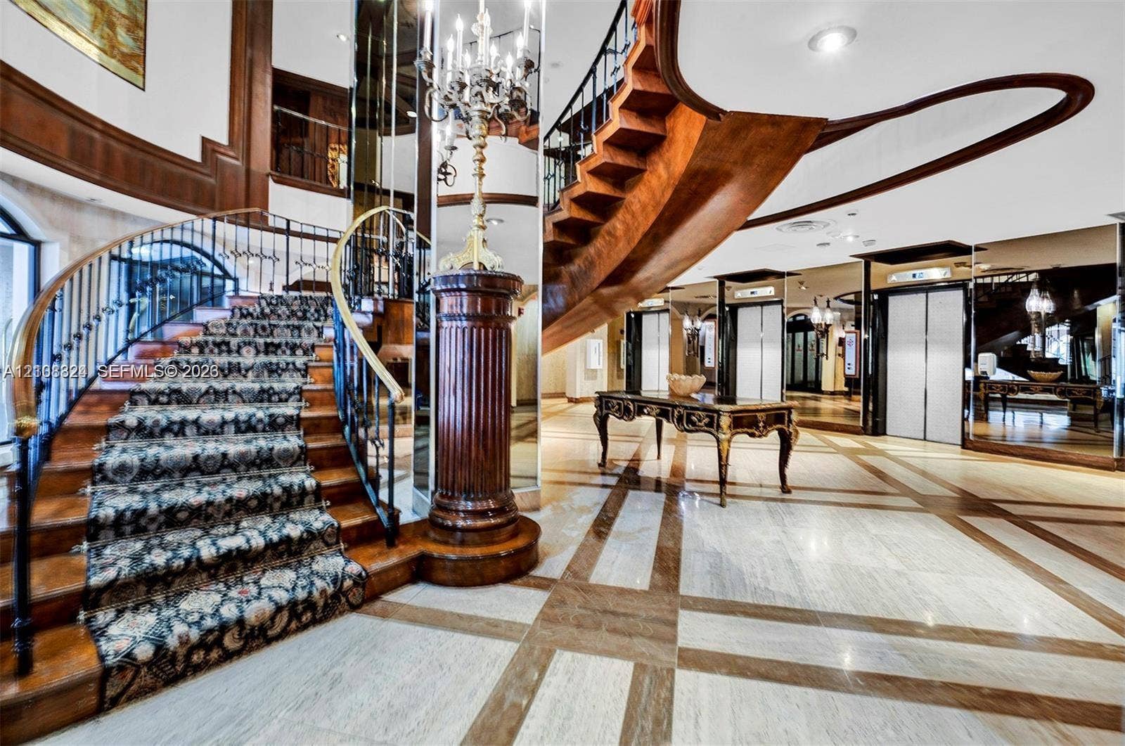 6039 Collins Avenue, #1208, Miami Beach, FL 33140 Grand foyer featuring a dual-tone stone floor, a sweeping staircase with custom metal railing, full-height wall mirrors, and recessed lighting