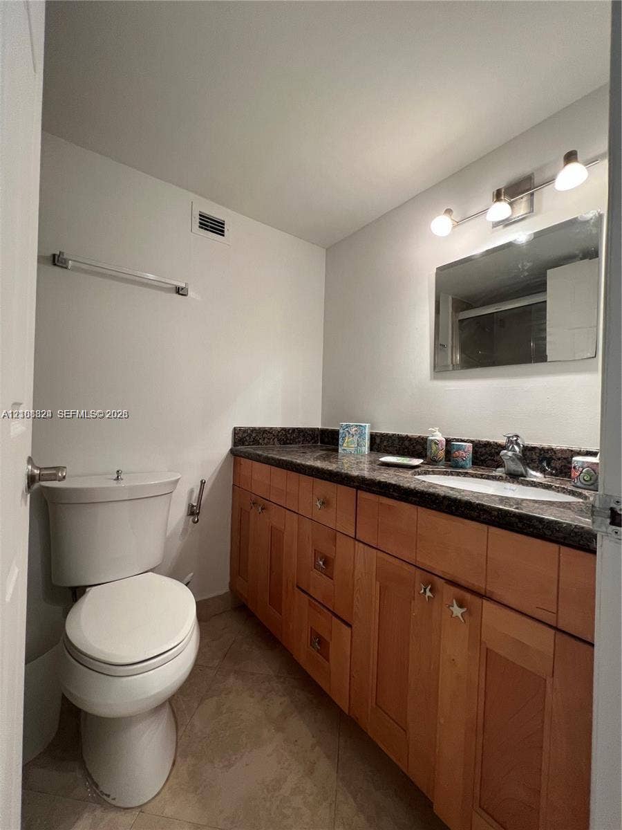 6039 Collins Avenue, #1208, Miami Beach, FL 33140 Bathroom featuring a stone-surface vanity with an integrated oval sink, natural wood-finish cabinetry, a framed wall mirror, and tile flooring