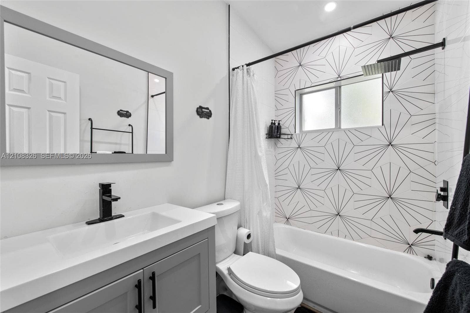 Bathroom featuring a vanity with a rectangular sink, matte black faucet, gray cabinetry, and geometric patterned tile shower surround with a rain-style shower head