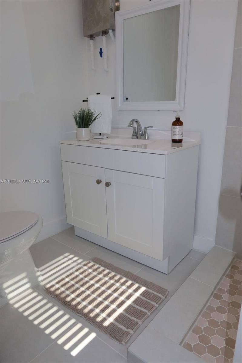 10450 SW 166th Terrace, #0, Miami, Miami, FL 33157 White shaker-style vanity with a solid surface countertop, integrated sink, chrome faucet, wall-mounted mirror, and hexagon-patterned floor tile