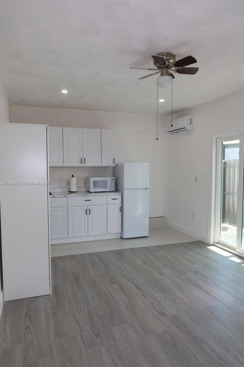 10450 SW 166th Terrace, #0, Miami, Miami, FL 33157 Kitchenette featuring white shaker-style cabinetry, stone-finish countertops, wood-finish flooring, a wall-mounted climate control unit, and a sliding glass door