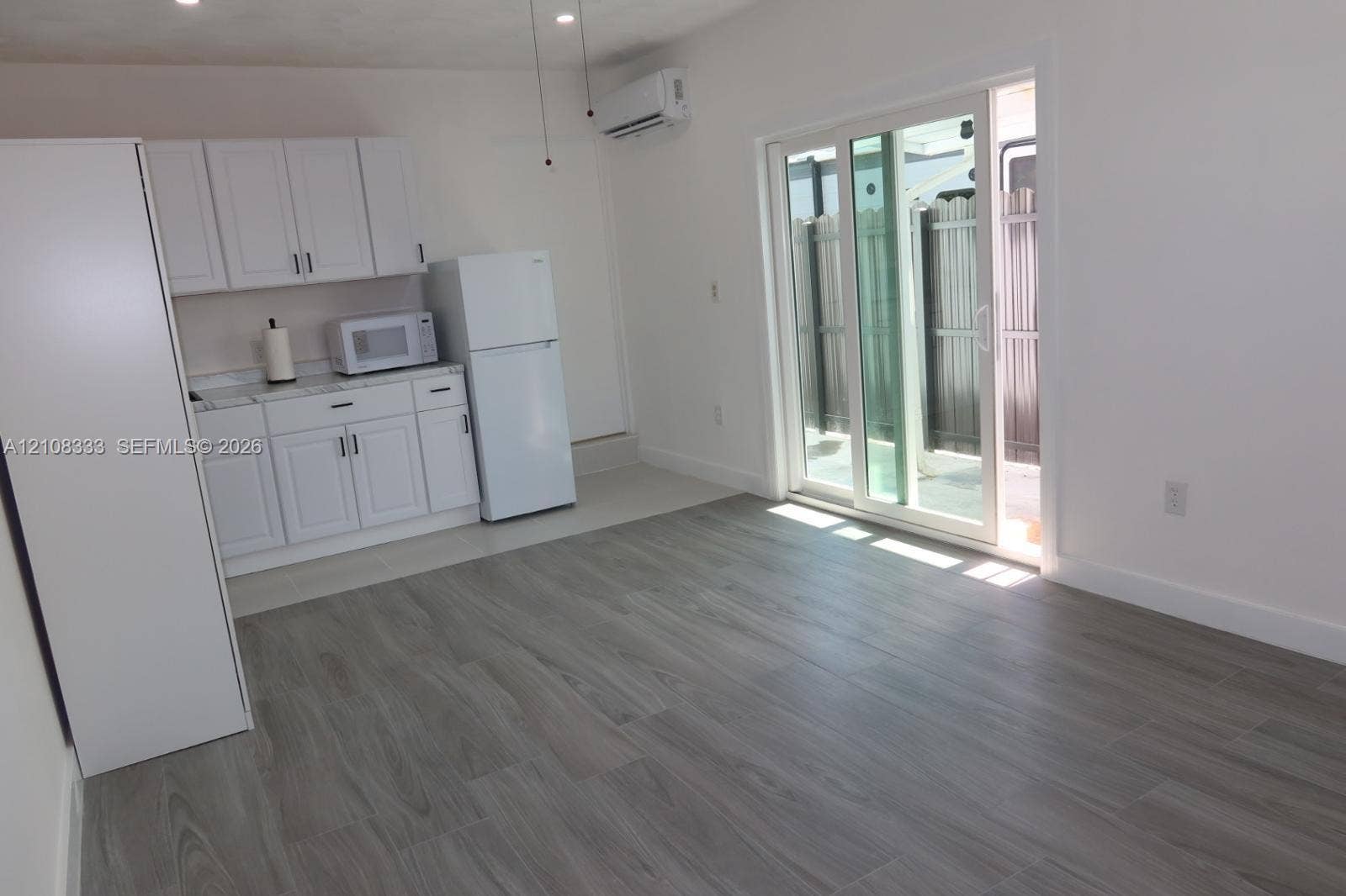 10450 SW 166th Terrace, #0, Miami, Miami, FL 33157 White cabinetry, wood-finish flooring, wall-mounted mini-split HVAC unit, and glass sliding doors