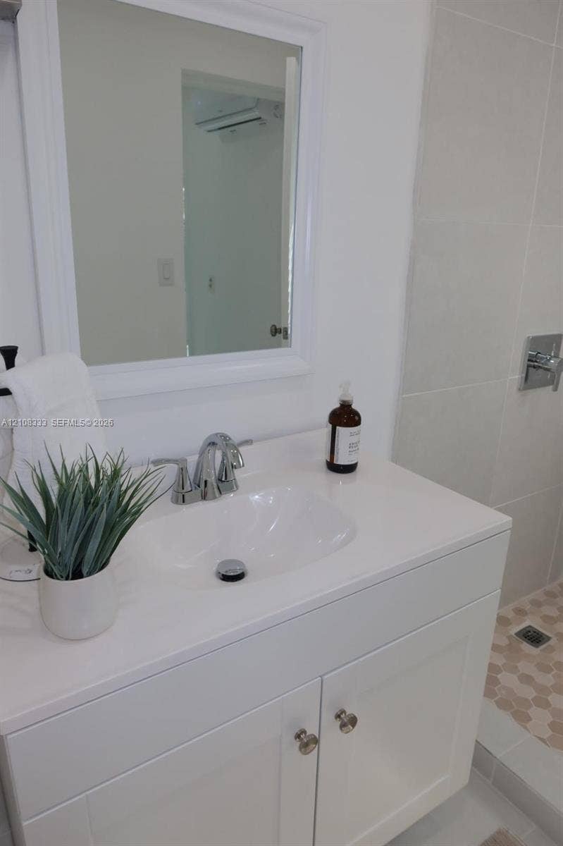 10450 SW 166th Terrace, #0, Miami, Miami, FL 33157 White vanity with a rectangular countertop, integrated basin, chrome faucet, and framed wall mirror, complemented by a walk-in shower with large-format wall tile and hexagonal floor tile