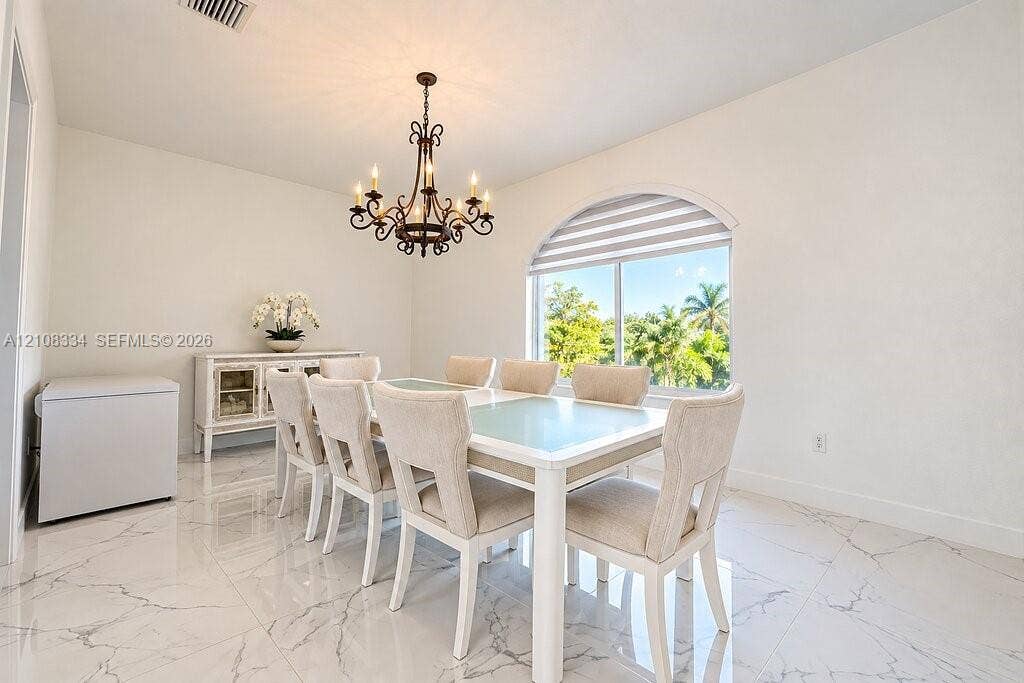 Dining area featuring large-format stone-patterned floor tile, an ornate wrought-iron chandelier, and a prominent arched window with a roller shade