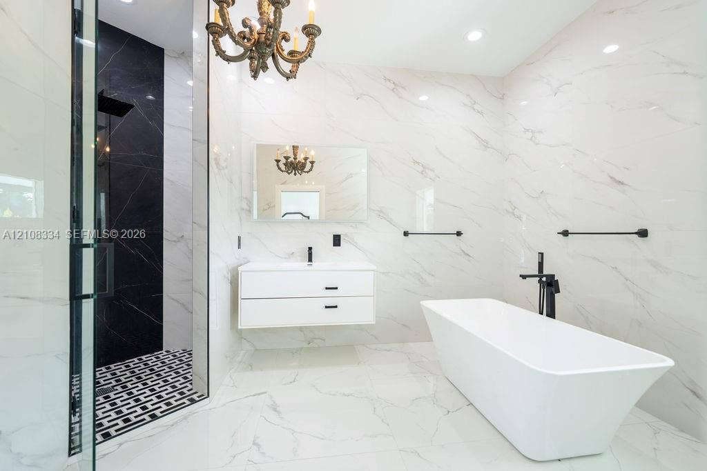 Bathroom featuring large-format veined tile, floating double-drawer vanity, freestanding soaking tub with matte black floor-mounted faucet, and glass-enclosed shower with contrasting tile inlay