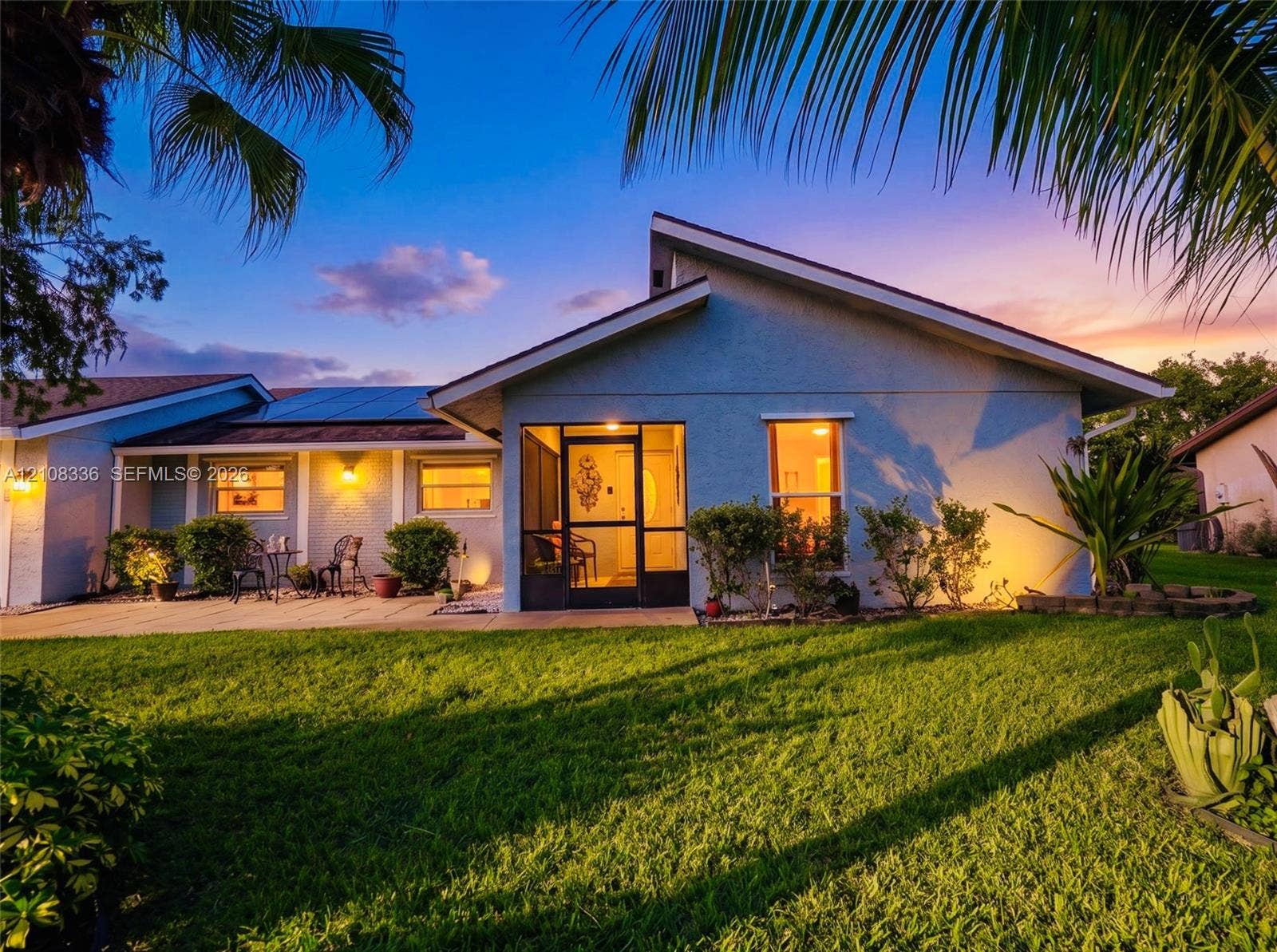 6311 Hitchin Post Way, Delray Beach, FL 33484 Single-story exterior featuring a screened-in entry, roof-integrated solar panels, stucco siding, and a paved patio area
