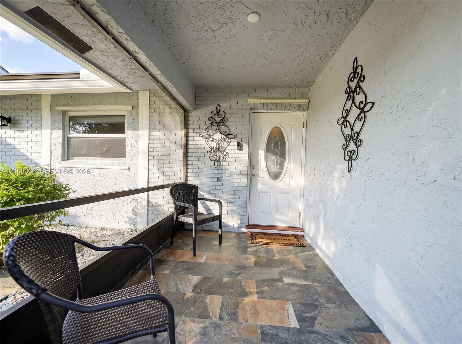 6311 Hitchin Post Way, Delray Beach, FL 33484 Covered entryway featuring painted brick walls, multi-tonal stone flooring, and a glass-paneled entry door