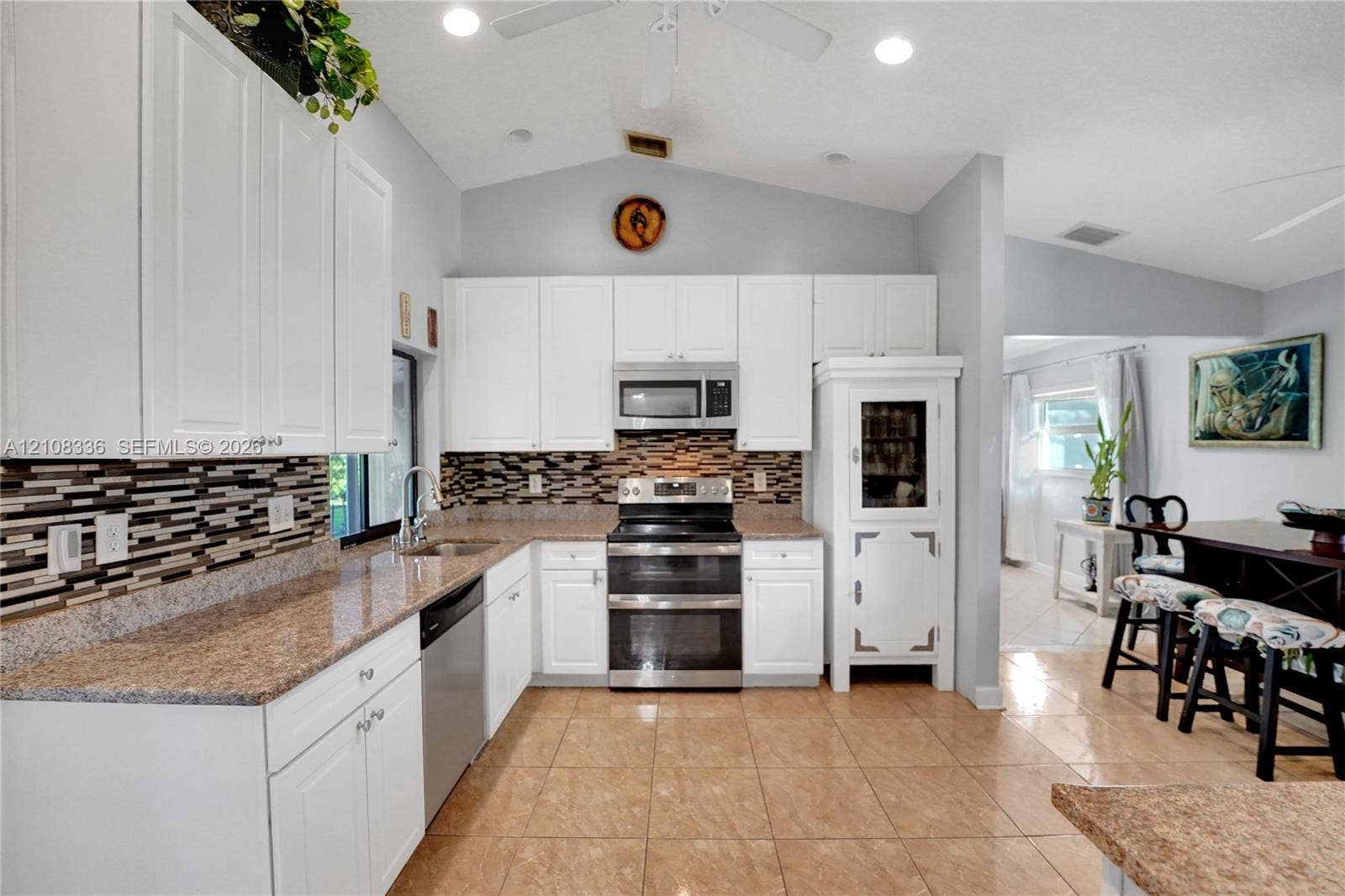 6311 Hitchin Post Way, Delray Beach, FL 33484 Kitchen featuring white cabinetry, stone-finish countertops, mosaic tile backsplash, stainless steel appliances, and tile flooring under a vaulted ceiling