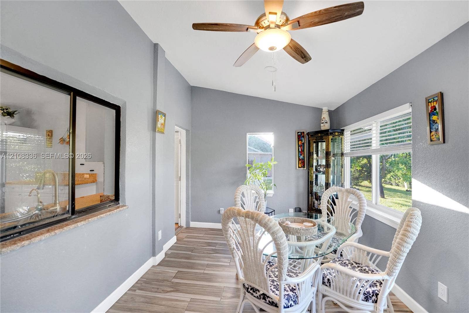 6311 Hitchin Post Way, Delray Beach, FL 33484 Vaulted ceilings featuring a centrally mounted ceiling fan, wood-finish tile flooring, a horizontal interior service window with a stone-finish ledge, and large windows providing natural light