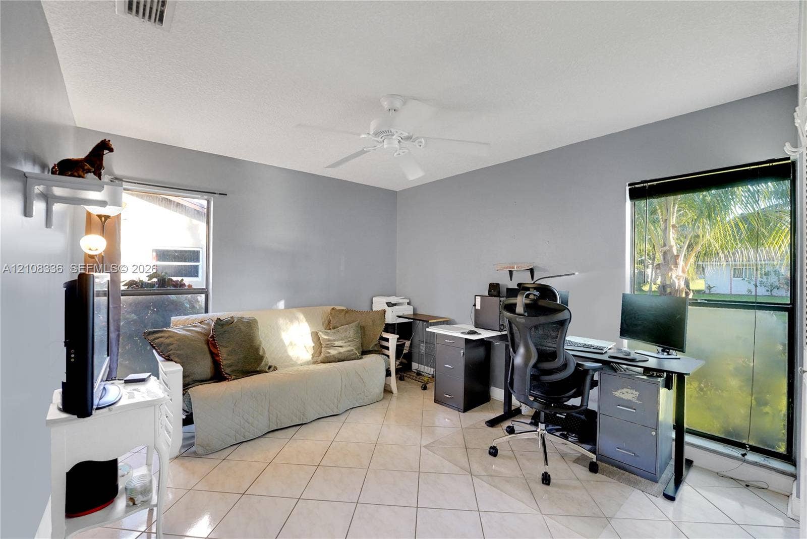 6311 Hitchin Post Way, Delray Beach, FL 33484 Neutral-toned interior featuring diagonal tile flooring, dual windows, a ceiling fan, and a wall-mounted shelving unit