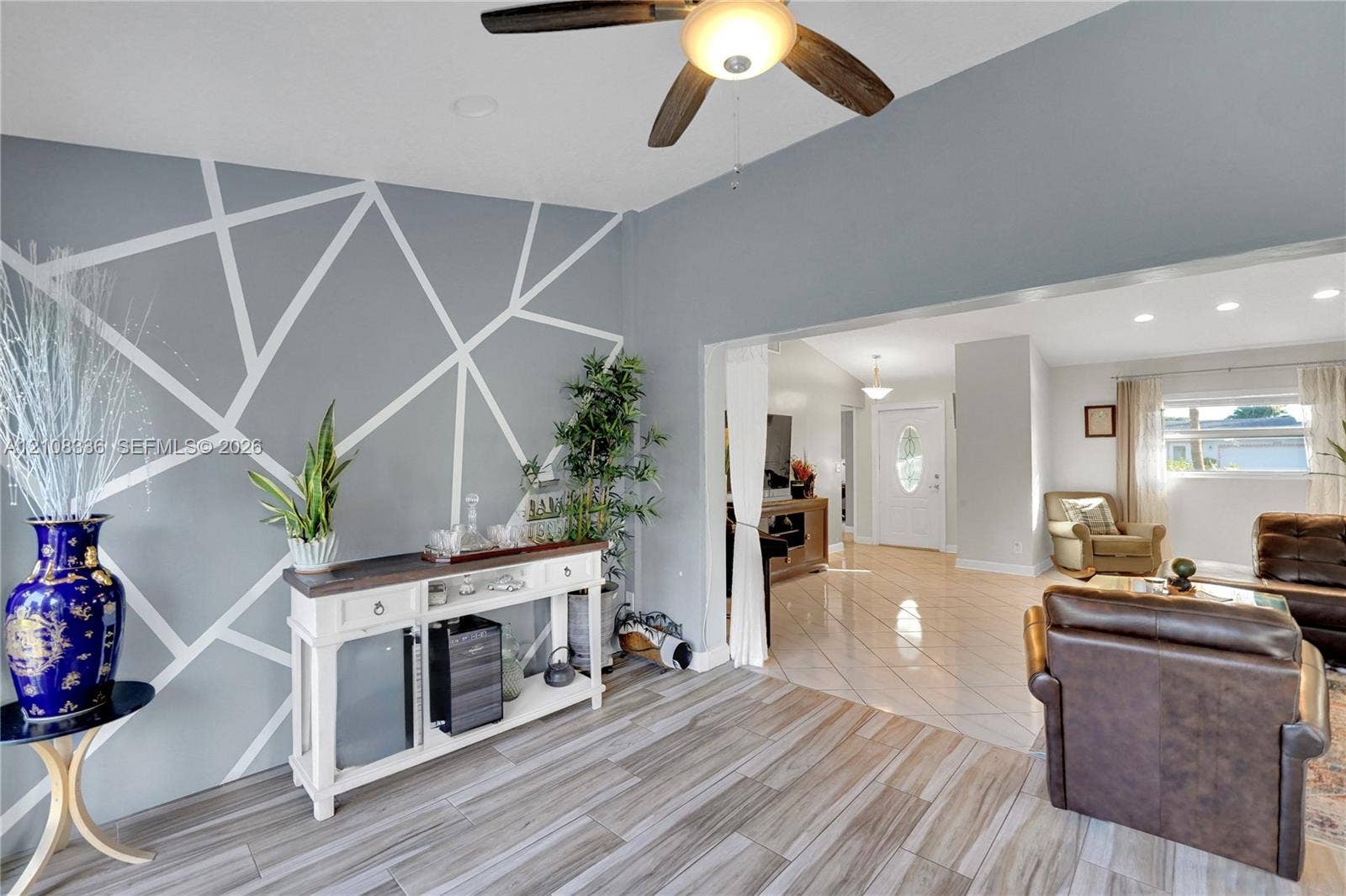 6311 Hitchin Post Way, Delray Beach, FL 33484 Geometric accent wall featuring a matte gray finish with white linear detailing, wood-finish flooring, and ceiling fan with integrated lighting