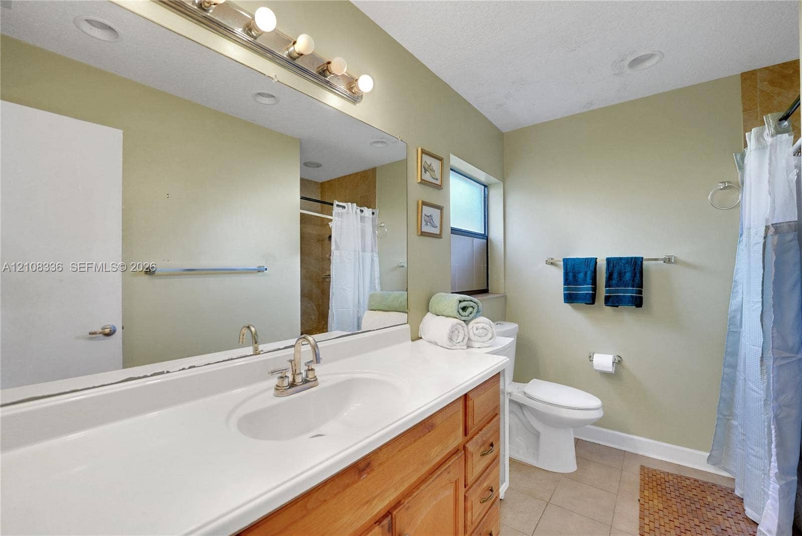 6311 Hitchin Post Way, Delray Beach, FL 33484 Bathroom featuring a wood vanity with an integrated countertop sink, wall-spanning mirror, multi-bulb vanity light, and tiled flooring
