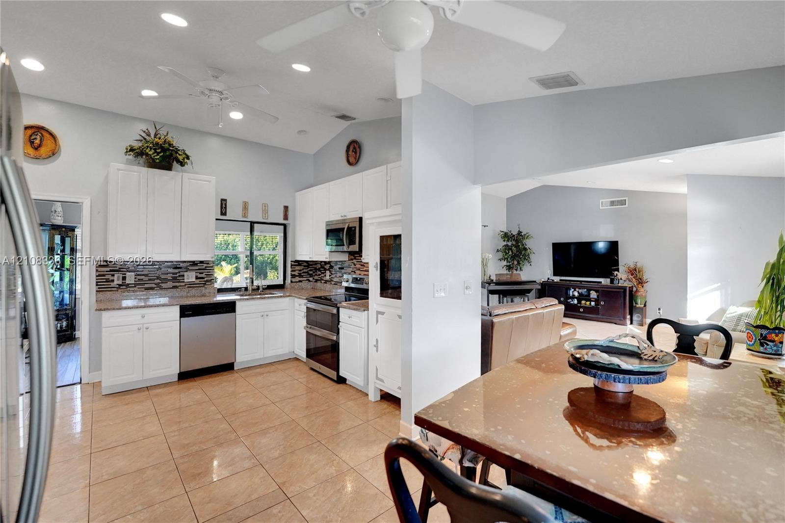 6311 Hitchin Post Way, Delray Beach, FL 33484 Kitchen featuring white cabinetry, stone-finish countertops, stainless steel appliances, a multi-tone decorative backsplash, and ceramic tile flooring under a vaulted ceiling