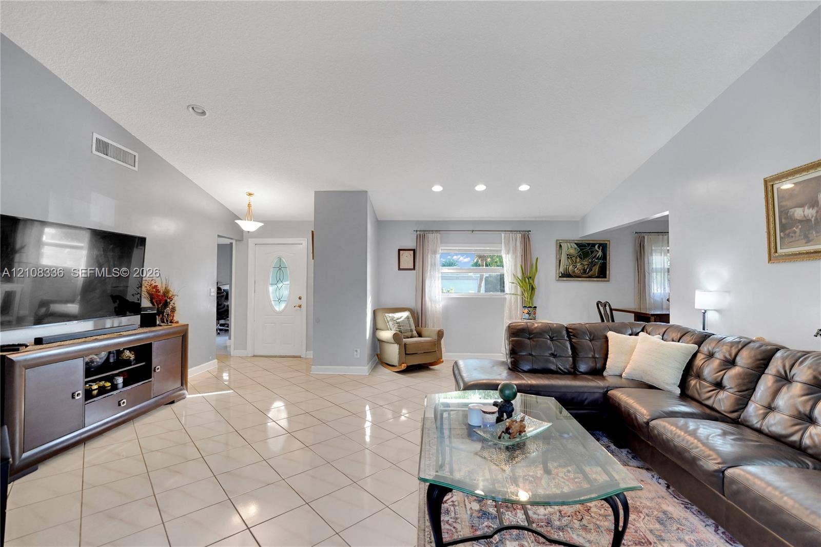 6311 Hitchin Post Way, Delray Beach, FL 33484 Open-concept living space featuring vaulted ceilings, light-toned ceramic tile flooring, recessed lighting, and a white entry door with an oval glass insert