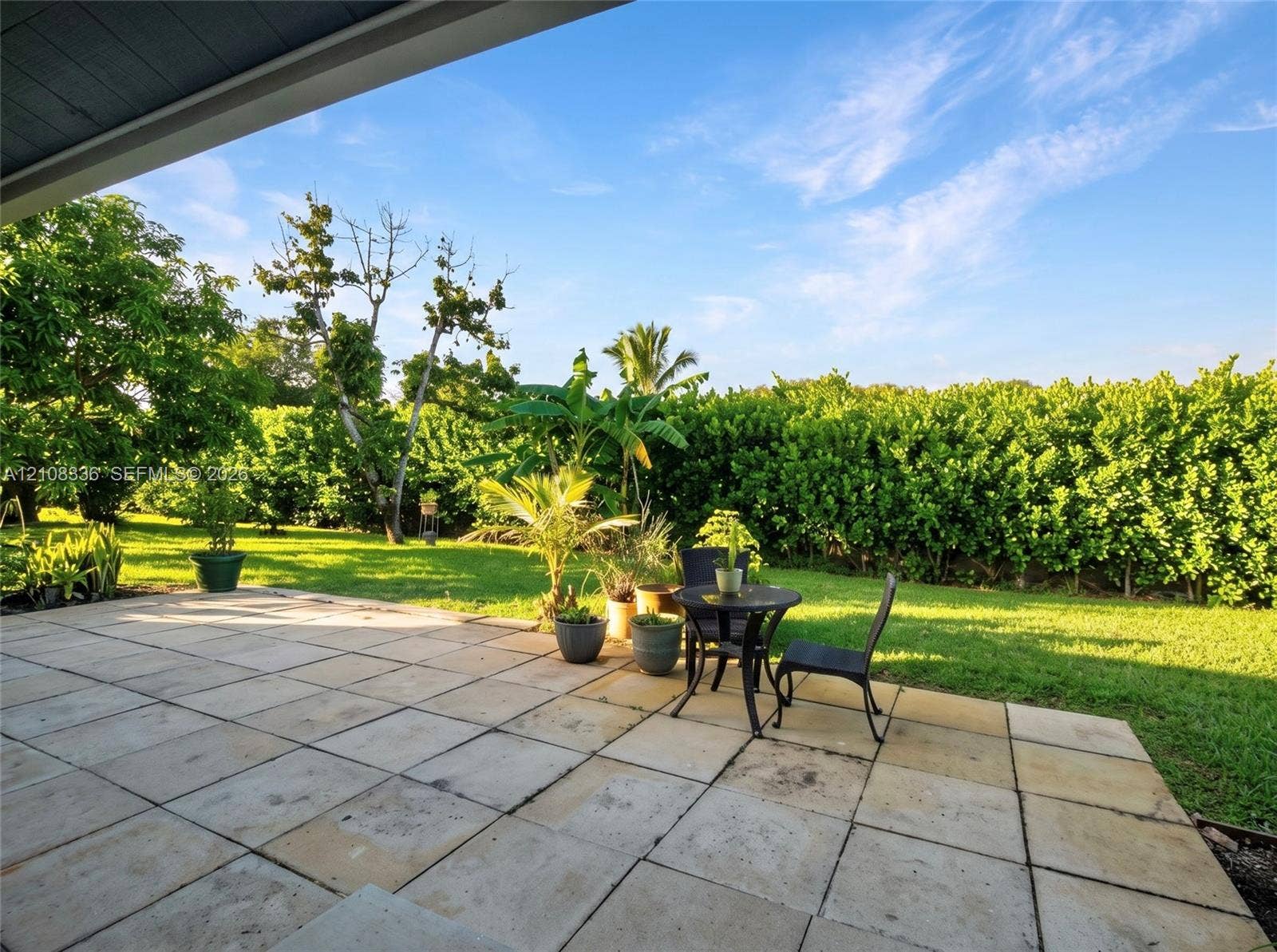 6311 Hitchin Post Way, Delray Beach, FL 33484 Covered patio featuring large-format stone pavers, manicured lawn, and mature privacy hedging
