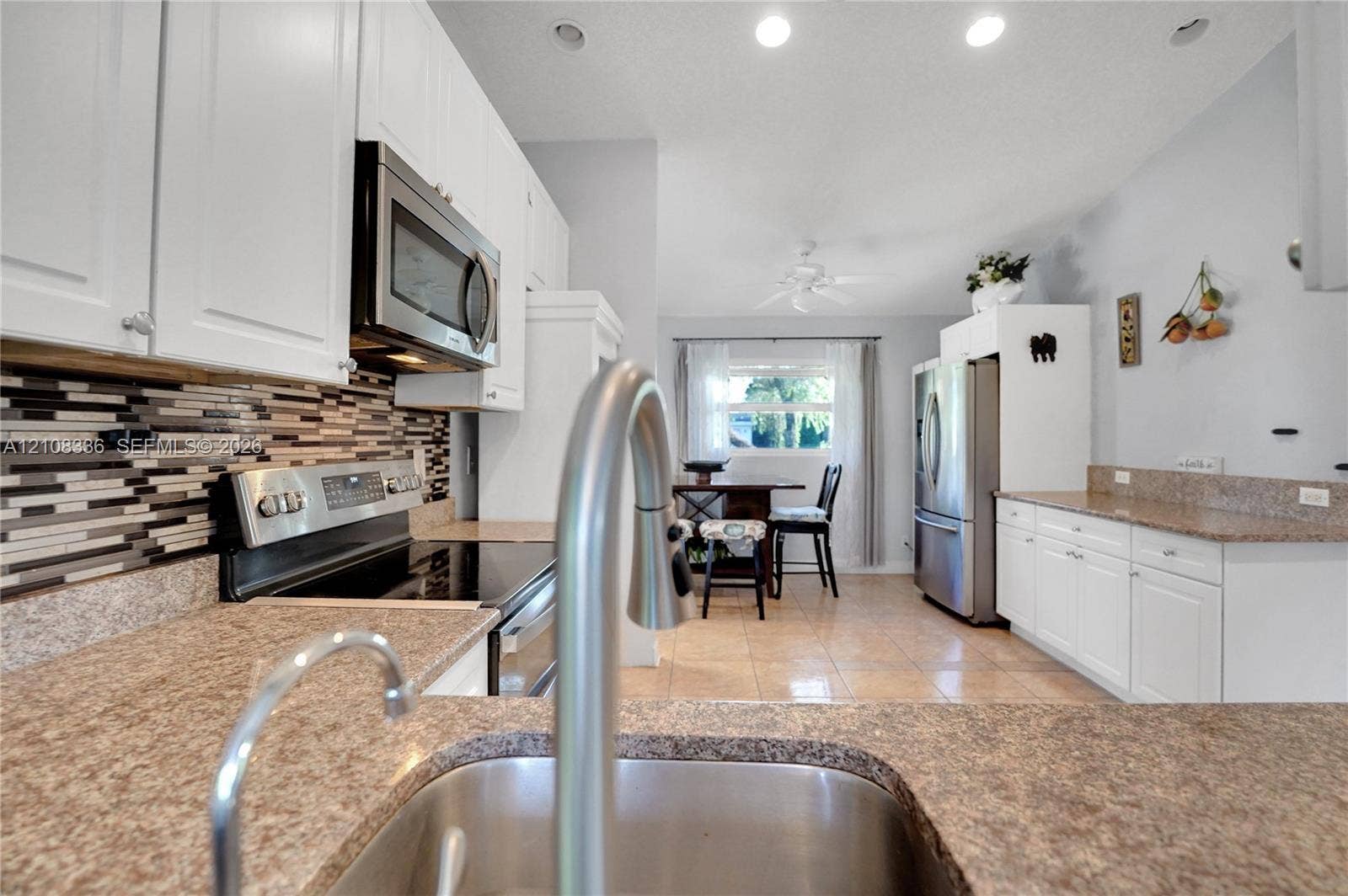 6311 Hitchin Post Way, Delray Beach, FL 33484 Kitchen featuring white cabinetry, stone-finish countertops, stainless steel appliances, a multi-tone tile backsplash, and tile flooring