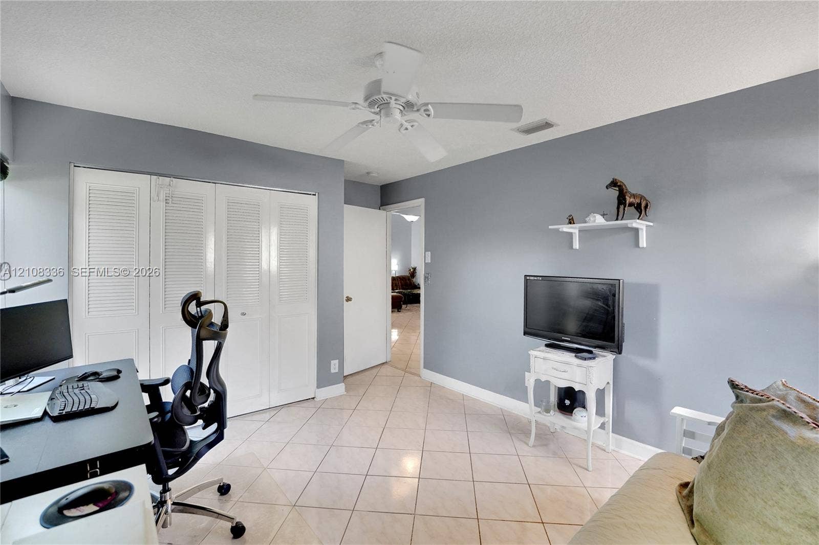 6311 Hitchin Post Way, Delray Beach, FL 33484 Room featuring neutral-toned walls, tile flooring, louvered bi-fold closet doors, a white ceiling fan, and a wall-mounted display shelf