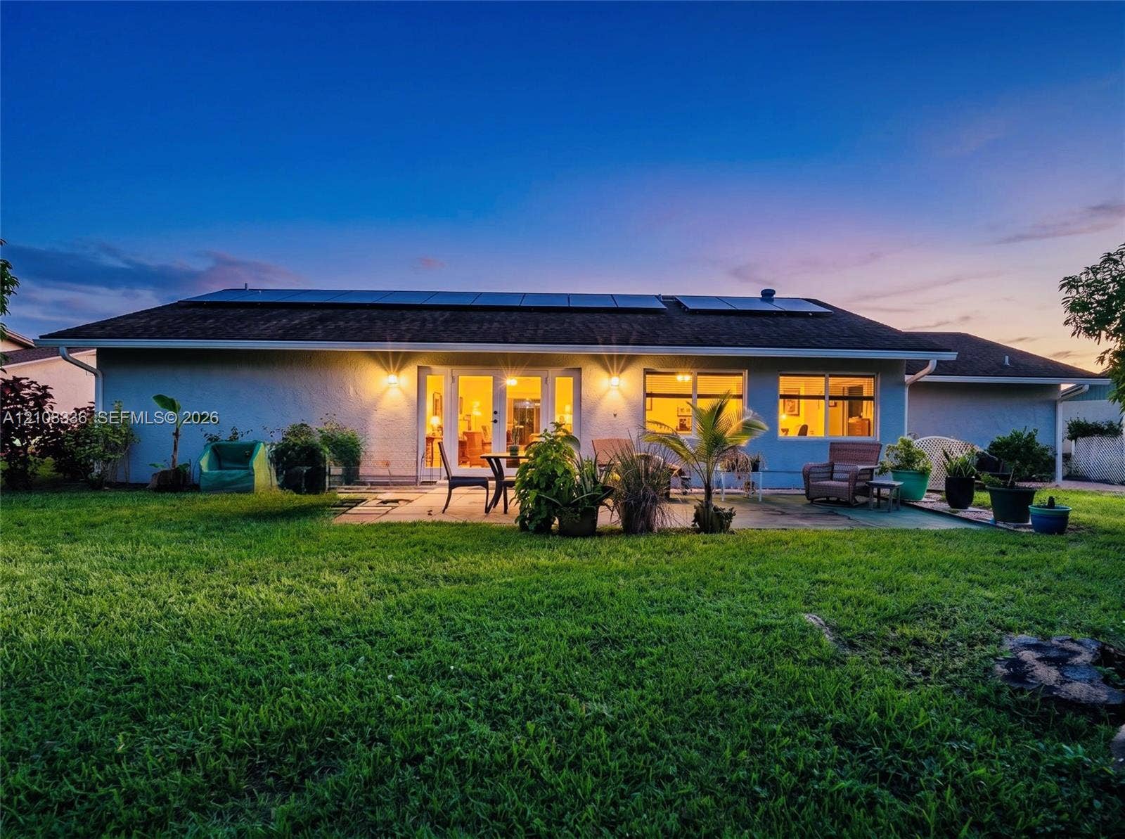 6311 Hitchin Post Way, Delray Beach, FL 33484 Single-story exterior featuring a concrete patio, roof-mounted solar panels, and large glass French doors