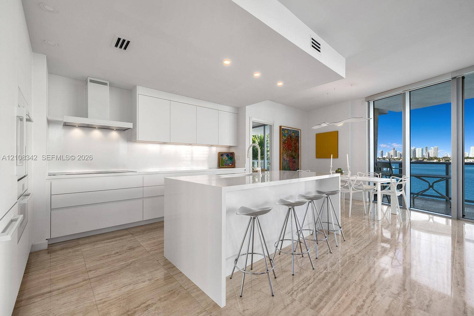 Contemporary kitchen featuring sleek flat-panel cabinetry, a waterfall-edge stone island, built-in stainless steel appliances, stone flooring, and floor-to-ceiling glass doors