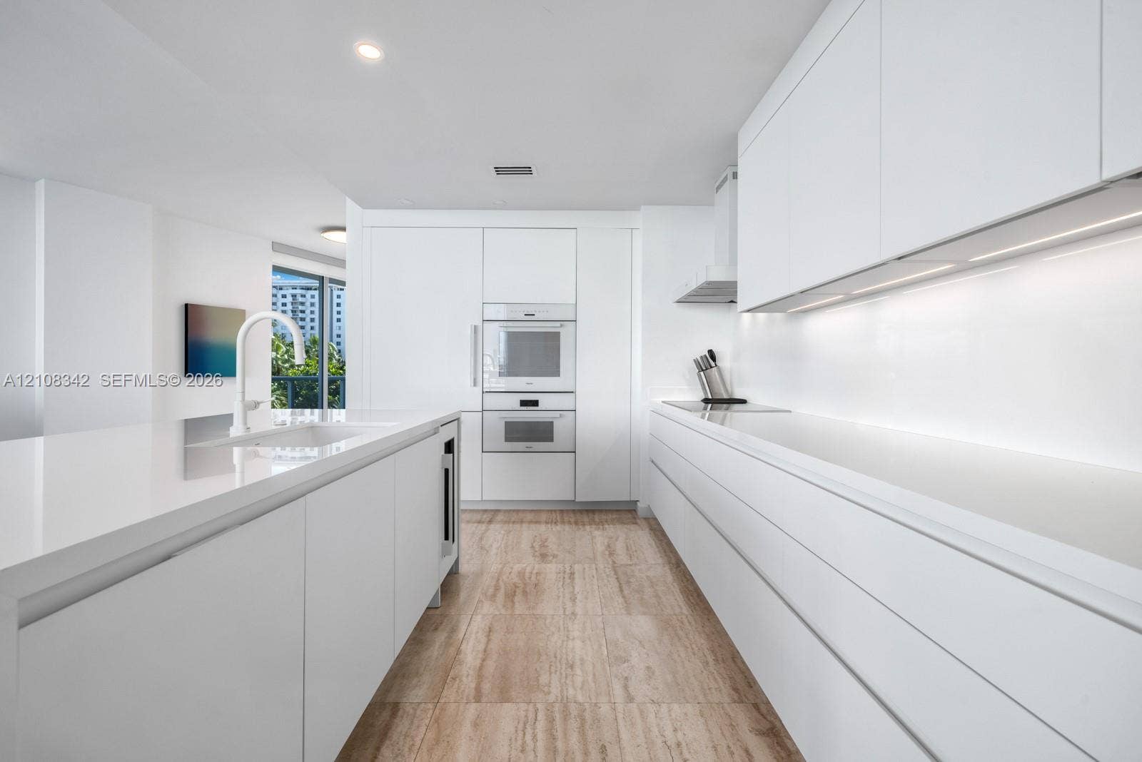 Minimalist kitchen featuring flat-panel cabinetry, white stone-surface countertops, built-in wall ovens, stone-finish flooring, and recessed ceiling lighting