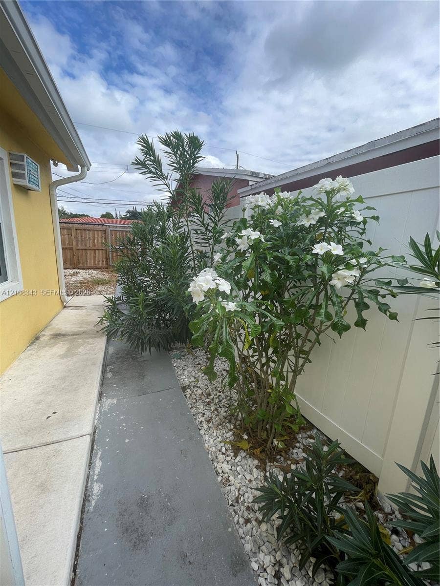 1935 Liberty Street, #3, Hollywood, Hollywood, FL 33020 Side yard featuring a poured concrete walkway, white vinyl fencing, and decorative stone landscaping with flowering shrubs